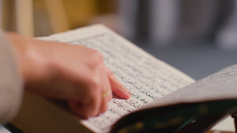 Close-Up-Of-Person-Turning-Pages-Of-The-Quran-On-Stand-At-Home